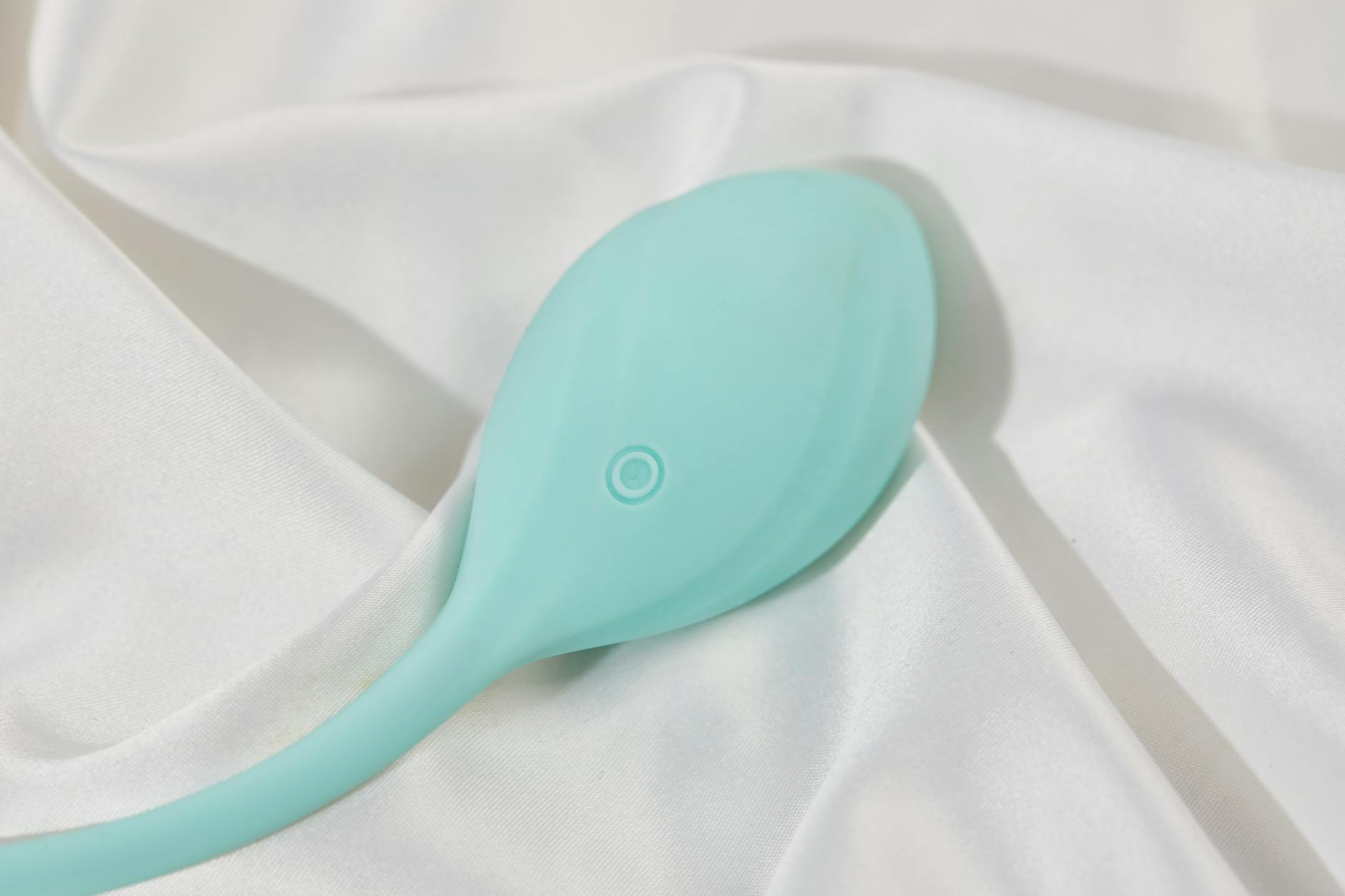 A teal silicone vibrator resting on soft white silk fabric, symbolizing gentle sensuality during recovery.
