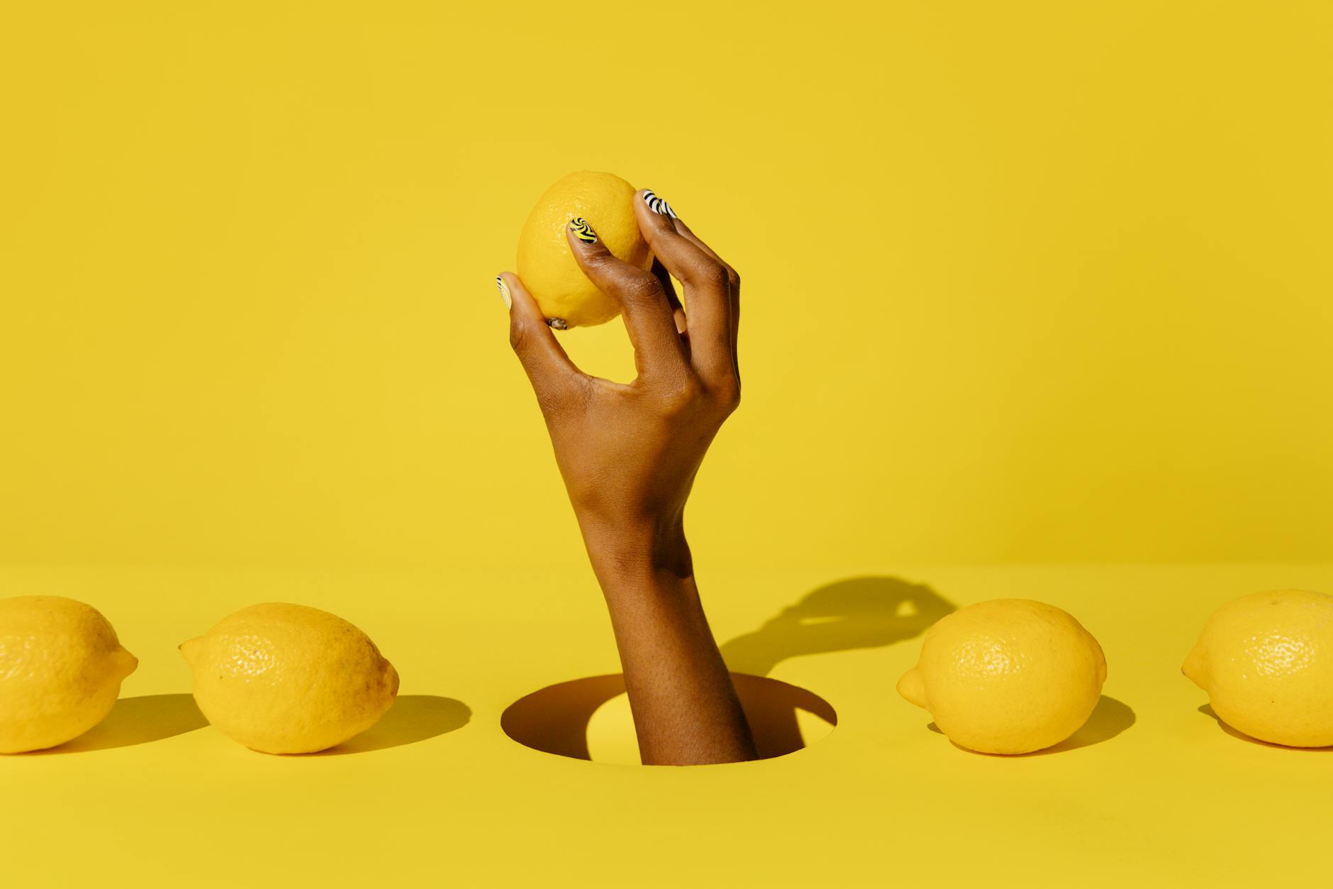 Hand holding a fresh lemon against a bright yellow background, representing the lemon vibrator's fresh approach to pleasure