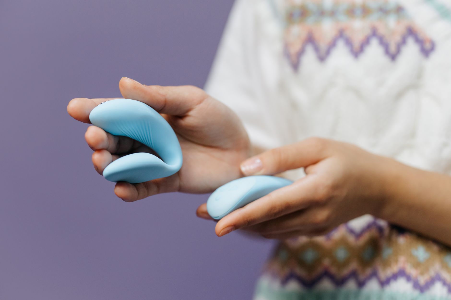 Deux mains tenant un vibromasseur bleu contre un fond pastel neutre