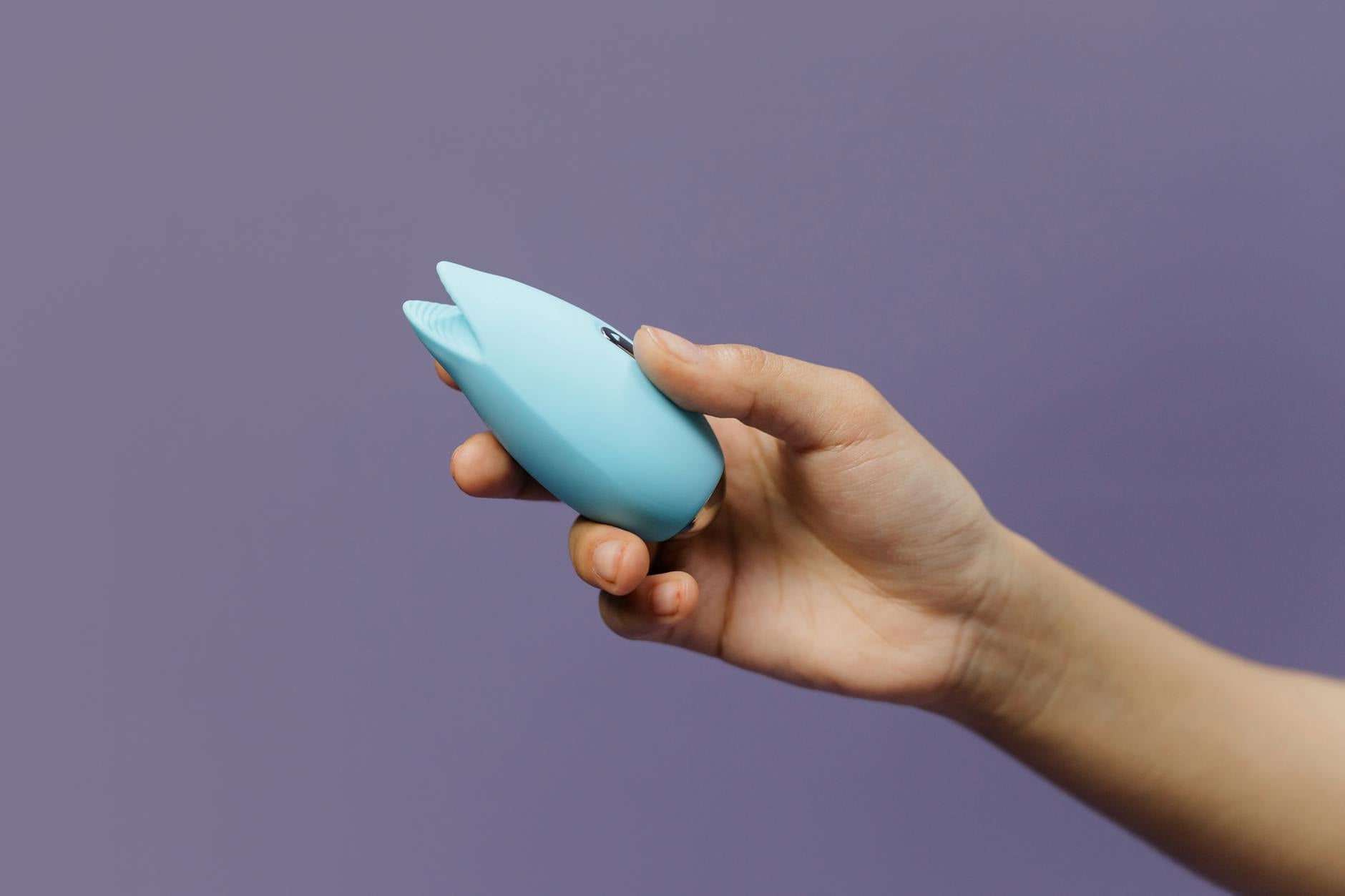 A blue silicone clitoral vibrator held gently in hand, representing controlled, intentional pleasure