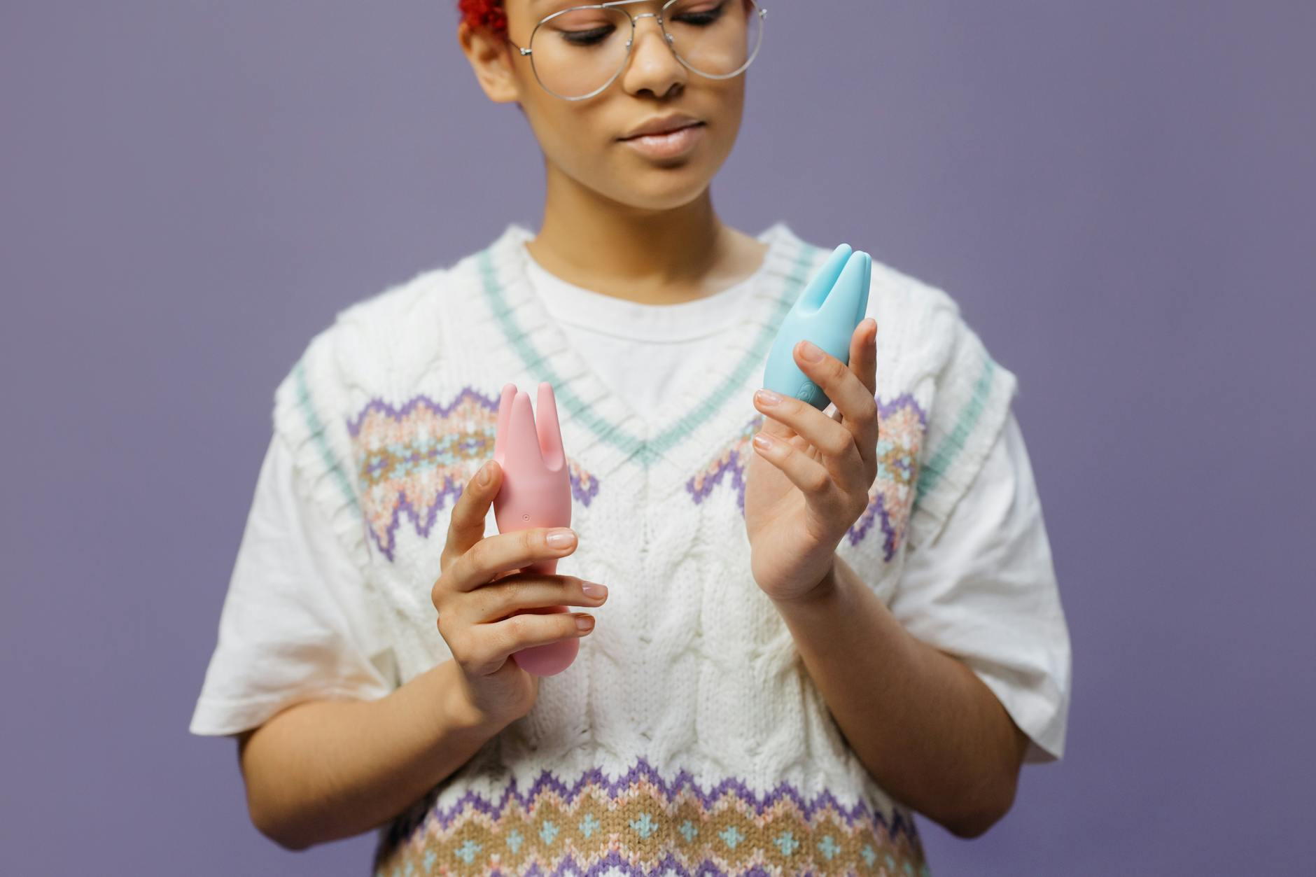 Woman holding a blue silicone vibrator with contemplative expression against a soft background