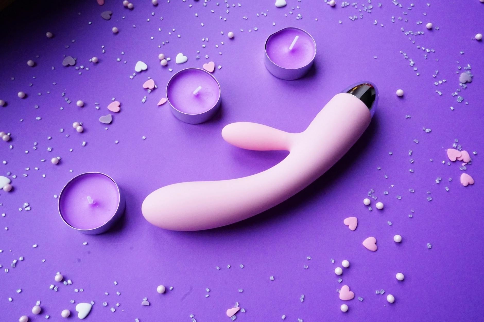 A pink lemon clitoral vibrator displayed on a soft purple background with heart confetti and candles for a romantic setup.